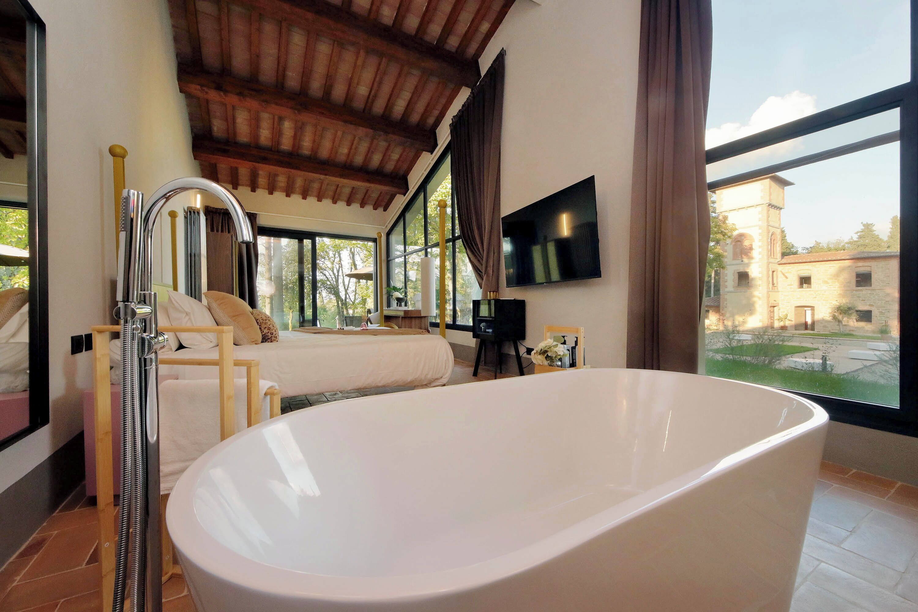 Un dormitorio moderno con una bañera grande, techo de madera y televisor en la pared.