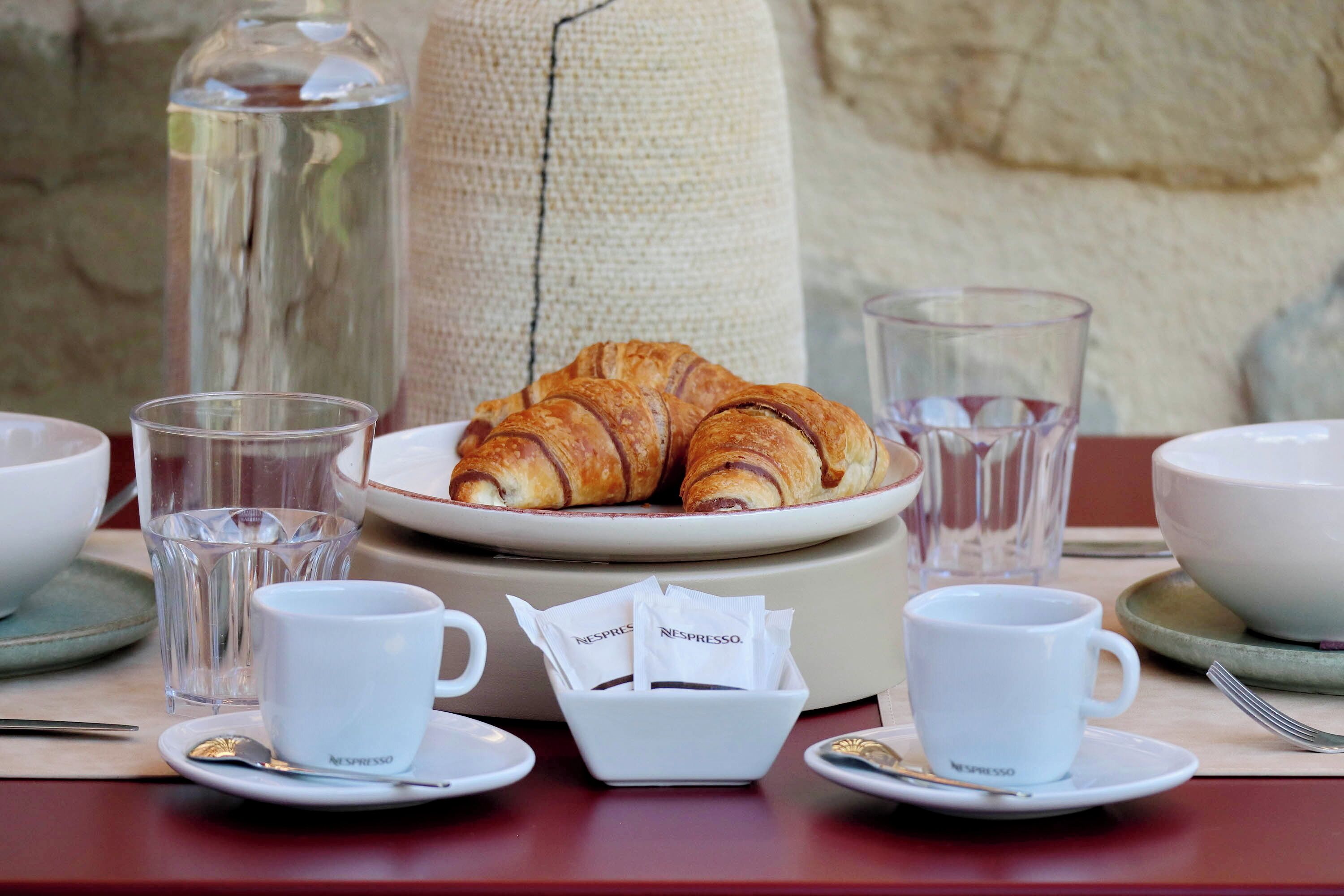 Een ontbijtje met croissants, koffiekopjes en een waterglas op tafel.