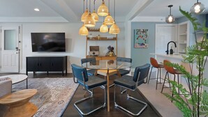 A modern dining area with a glass-top table, blue chairs, and a unique ceiling light fixture. - Harmony House (Nashville)