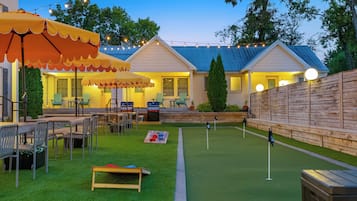 A backyard with a dining area, barbecue setup, and artificial turf.