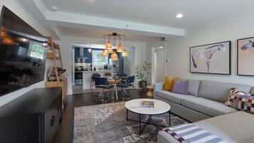 A modern living room with a sofa, coffee table, and a dining area with chairs and a table.