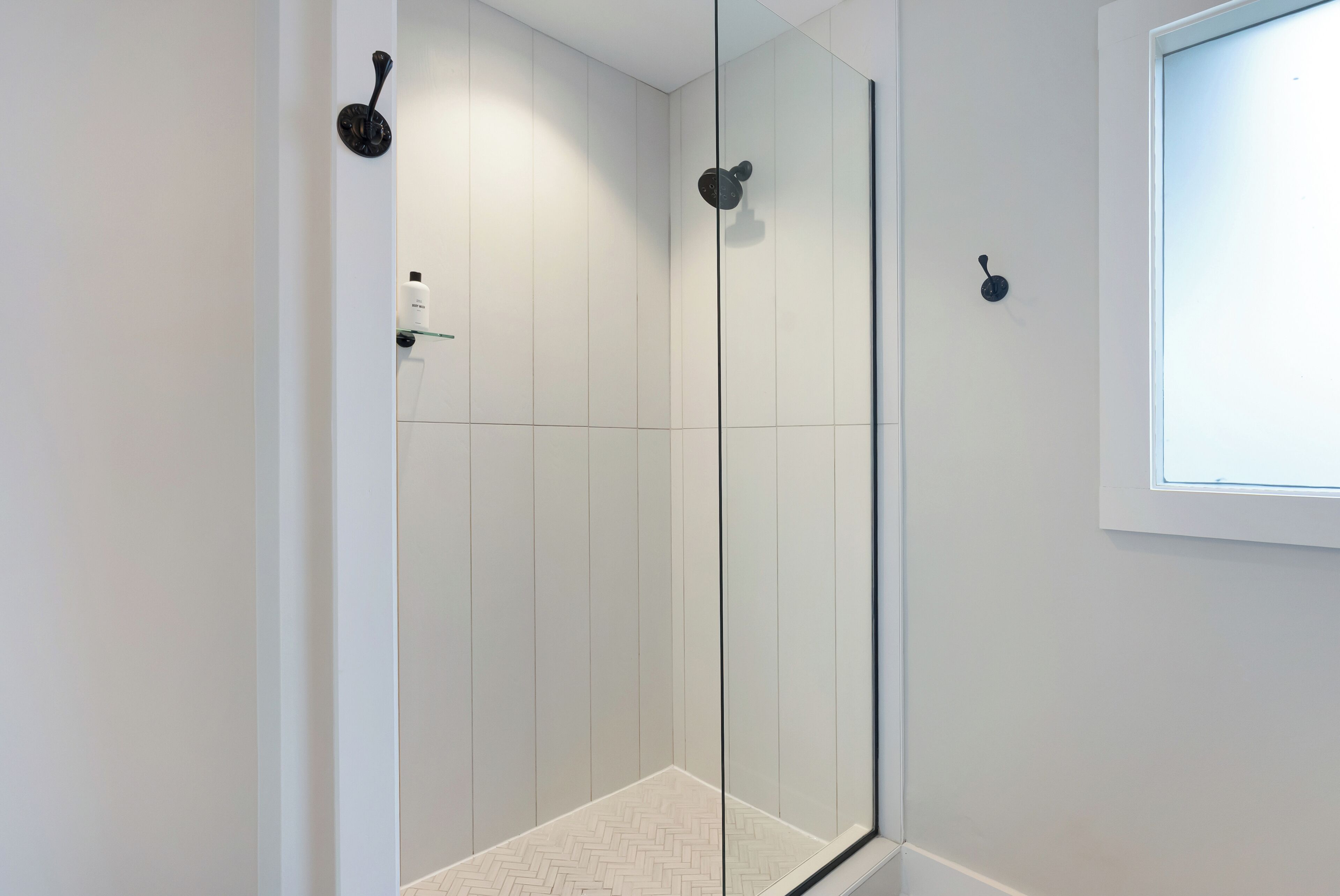 A modern shower with glass doors, a herringbone tile floor, and a window above the shower.