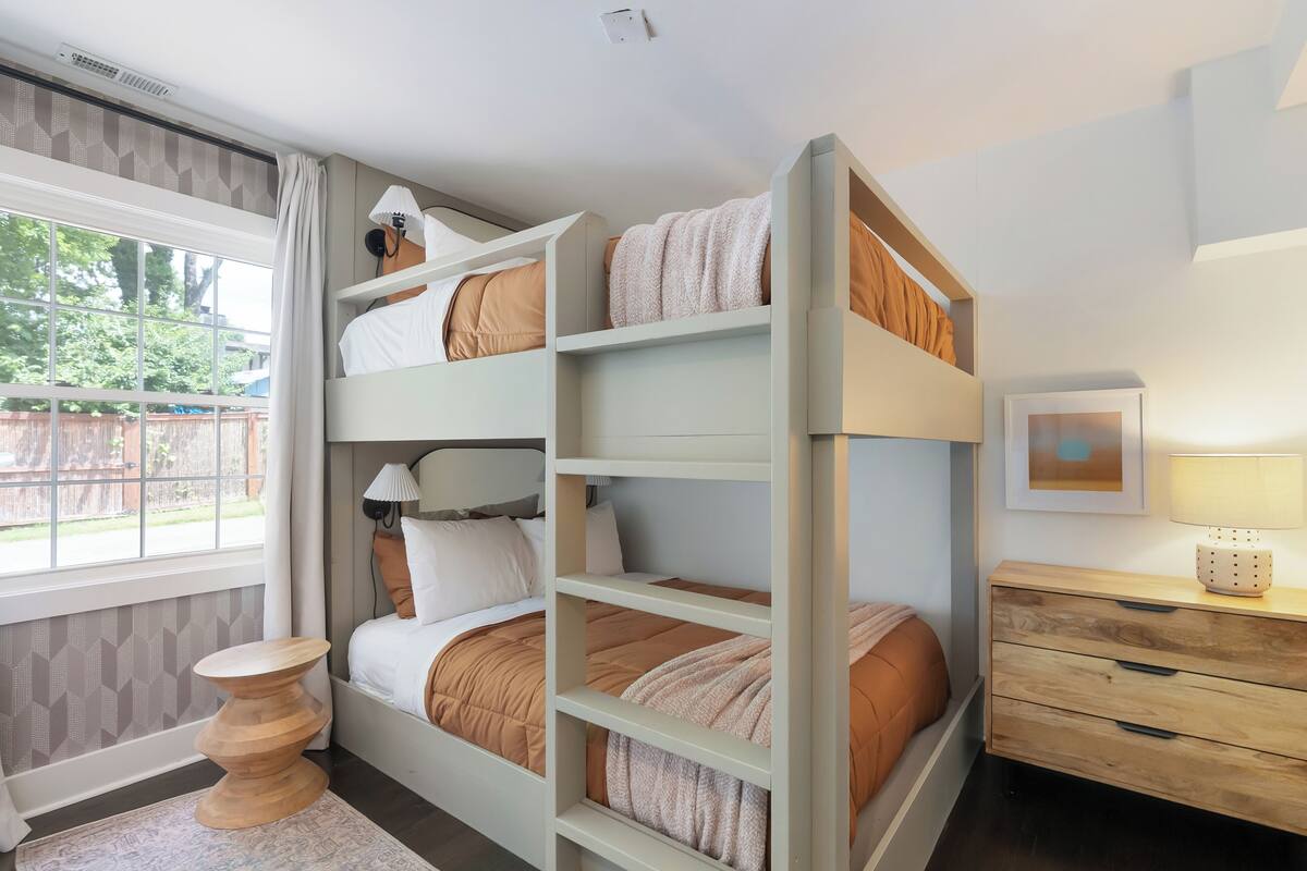 A bunk bed room with a desk, a lamp, and a window with curtains.