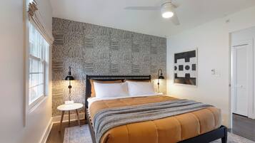 A bedroom with a bed, a ceiling fan, a window, and a wall with a patterned wallpaper.