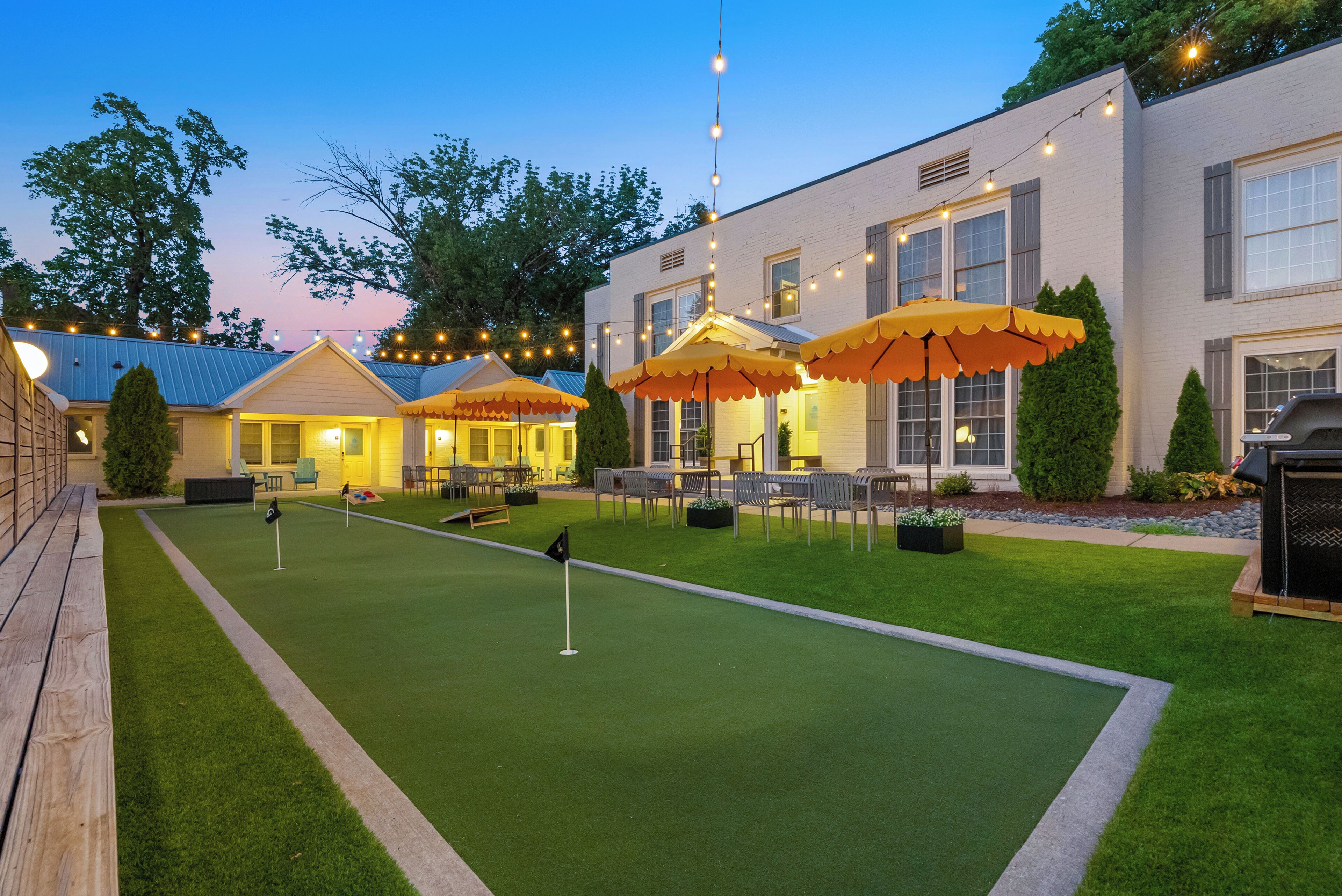A well-maintained outdoor area with artificial grass, a putting green, and outdoor seating under umbrellas.