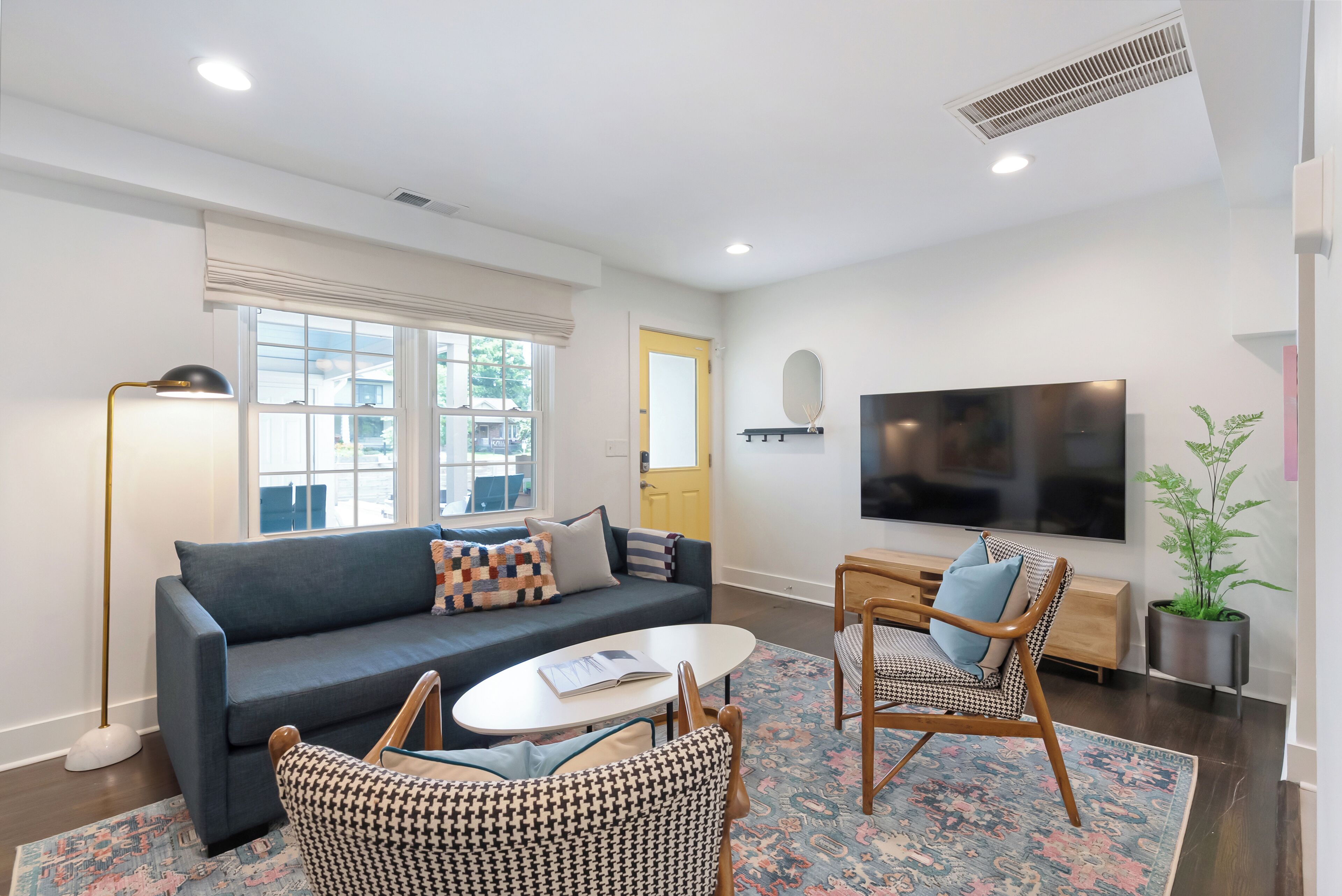 A modern living room with a sofa, chairs, a coffee table, a TV, and a potted plant.
