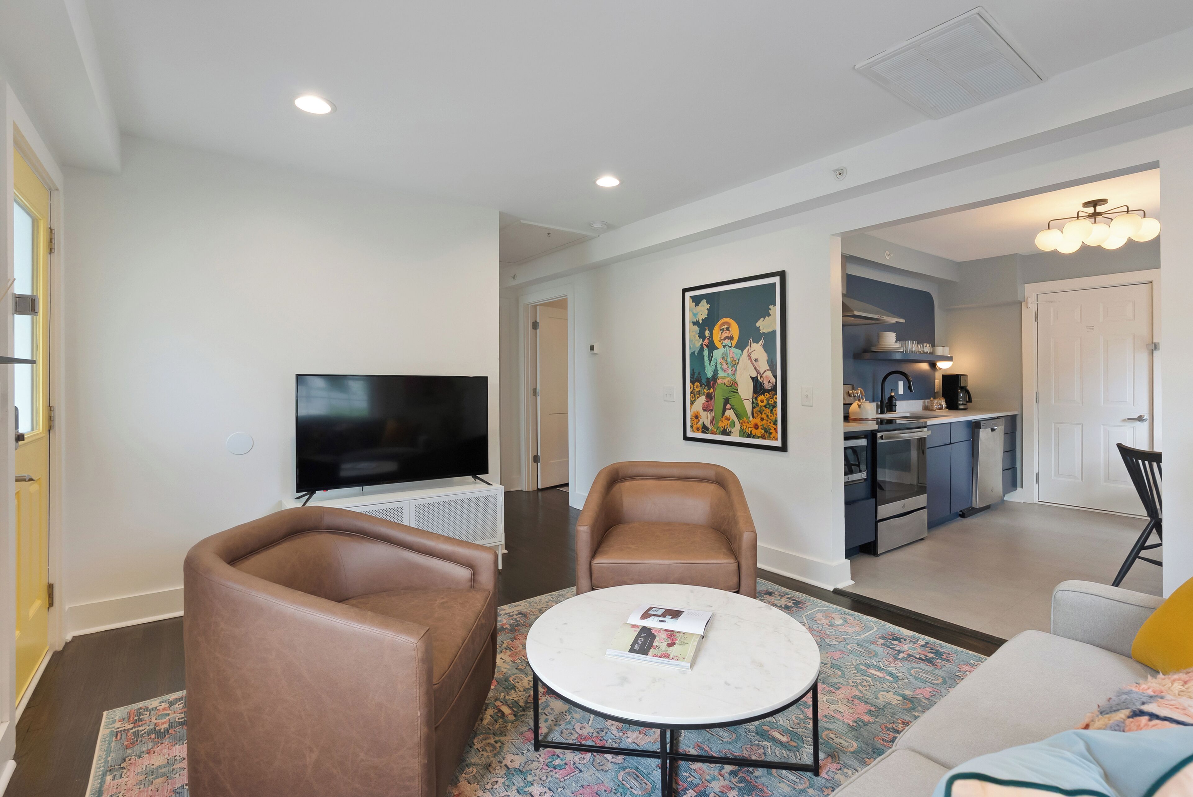 Una sala de estar moderna con un televisor de pantalla plana, sillones de cuero, una mesa de centro y una alfombra colorida.