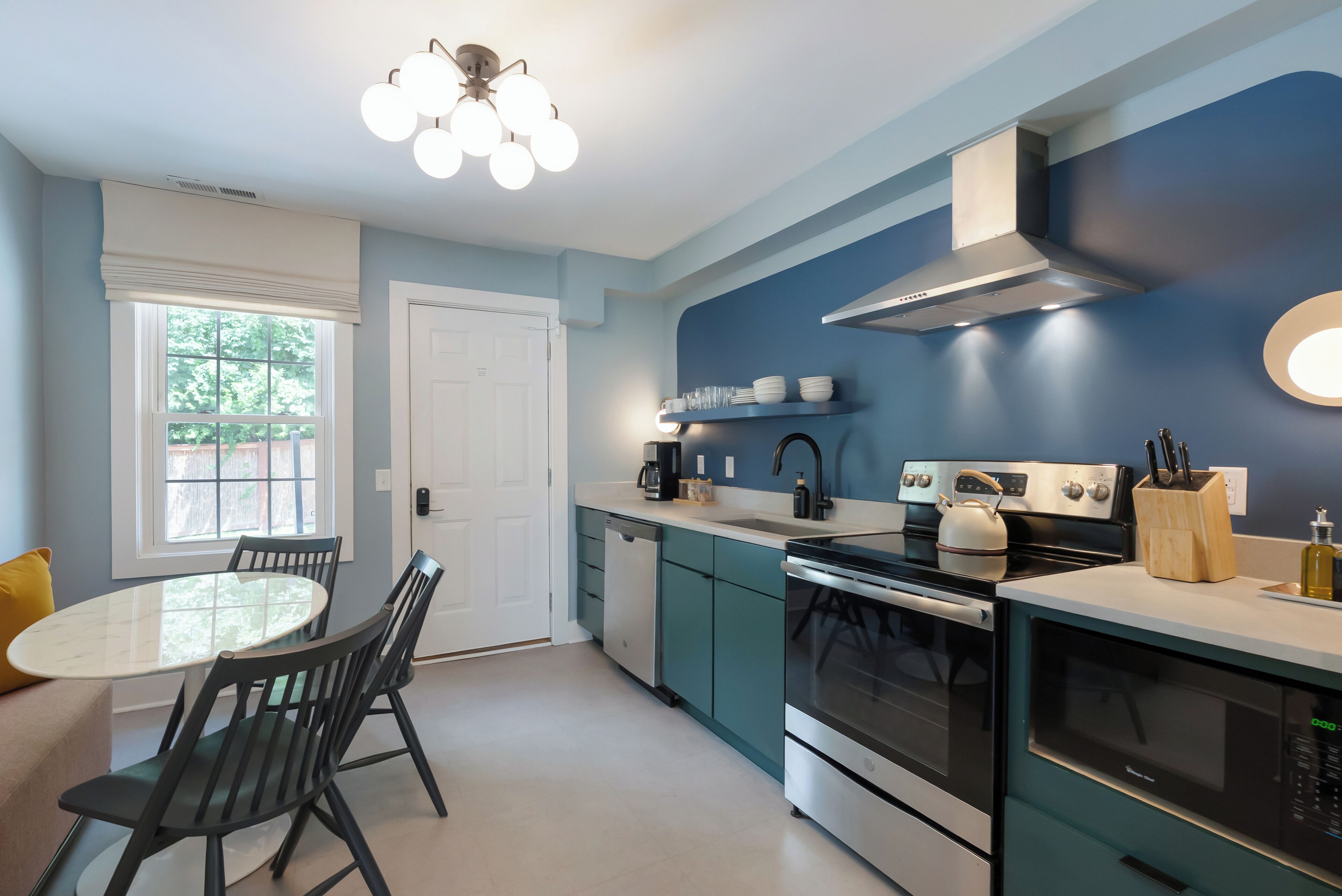 A modern kitchen with teal cabinets, stainless steel appliances, and a dining area with a round table and chairs.