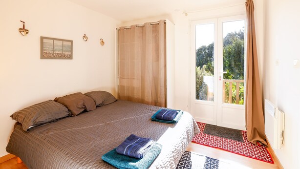 Quarto com cama, janela e vista para o verde.