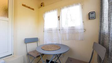 A small room with a round table, two chairs, a window with lace curtains, and a thermostat on the wall.