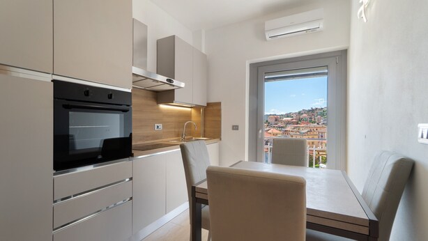Een moderne keuken met inbouwapparatuur, een eethoek met een tafel en stoelen, en een stadsgezicht door een raam.