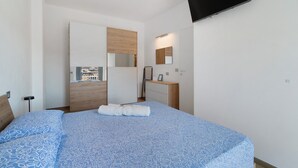 Een slaapkamer met een bed, een aan de muur bevestigde televisie, een houten deur en een raam.