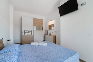 A bedroom with a bed, a TV mounted on the wall, a wooden door, and a window.