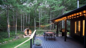 Eine Holzterrasse mit Grillplatz, einem Holzfass und Lichterketten.