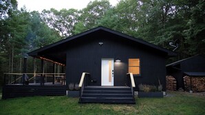 Eine schwarze Hütte mit weißer Tür, einer kleinen Veranda und einer Treppe, die zum Eingang führt.