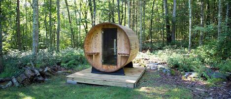 A wooden cylindrical structure with a door, situated on a wooden platform in a forest.