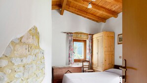 Ein Schlafzimmer mit Holzbalkendecke, einem Holzschrank, einem Schreibtisch, einem Stuhl und einem Bett.