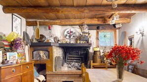 Eine rustikale Küche mit Kamin aus Backsteinen, Holzbalken und einem Esstisch mit Blumen in einer Vase.