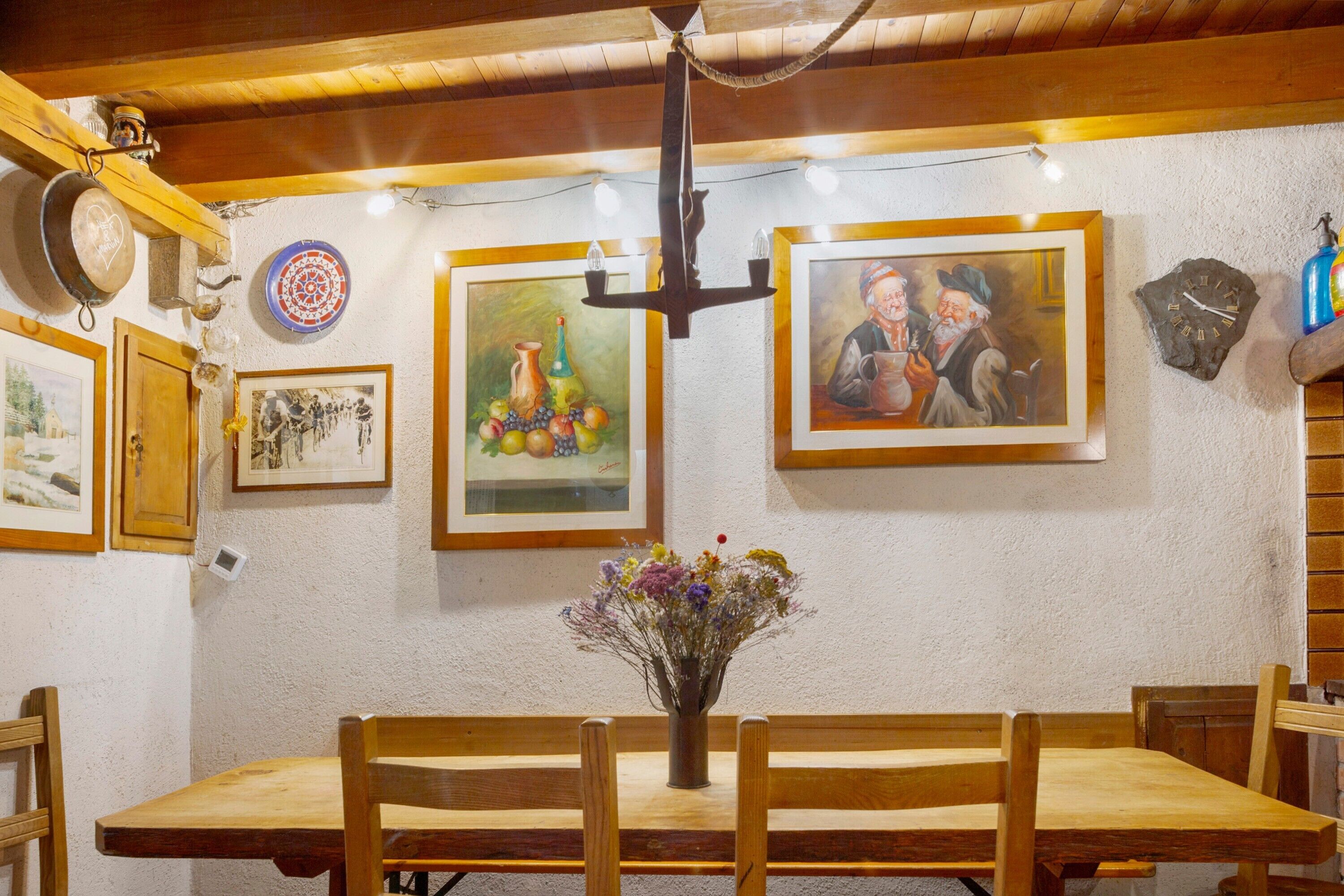 Zona pranzo con tavolo e sedie in legno, un vaso con fiori e diverse opere d'arte appese al muro.
