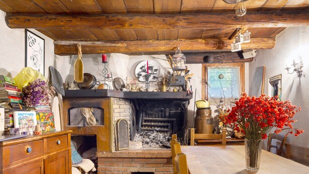 A rustic kitchen with a brick fireplace, wooden beams, and a dining table with a vase of flowers. - Room 'Camera 2' with Mountain View, Shared Garden and Wi-Fi (Arsiè)