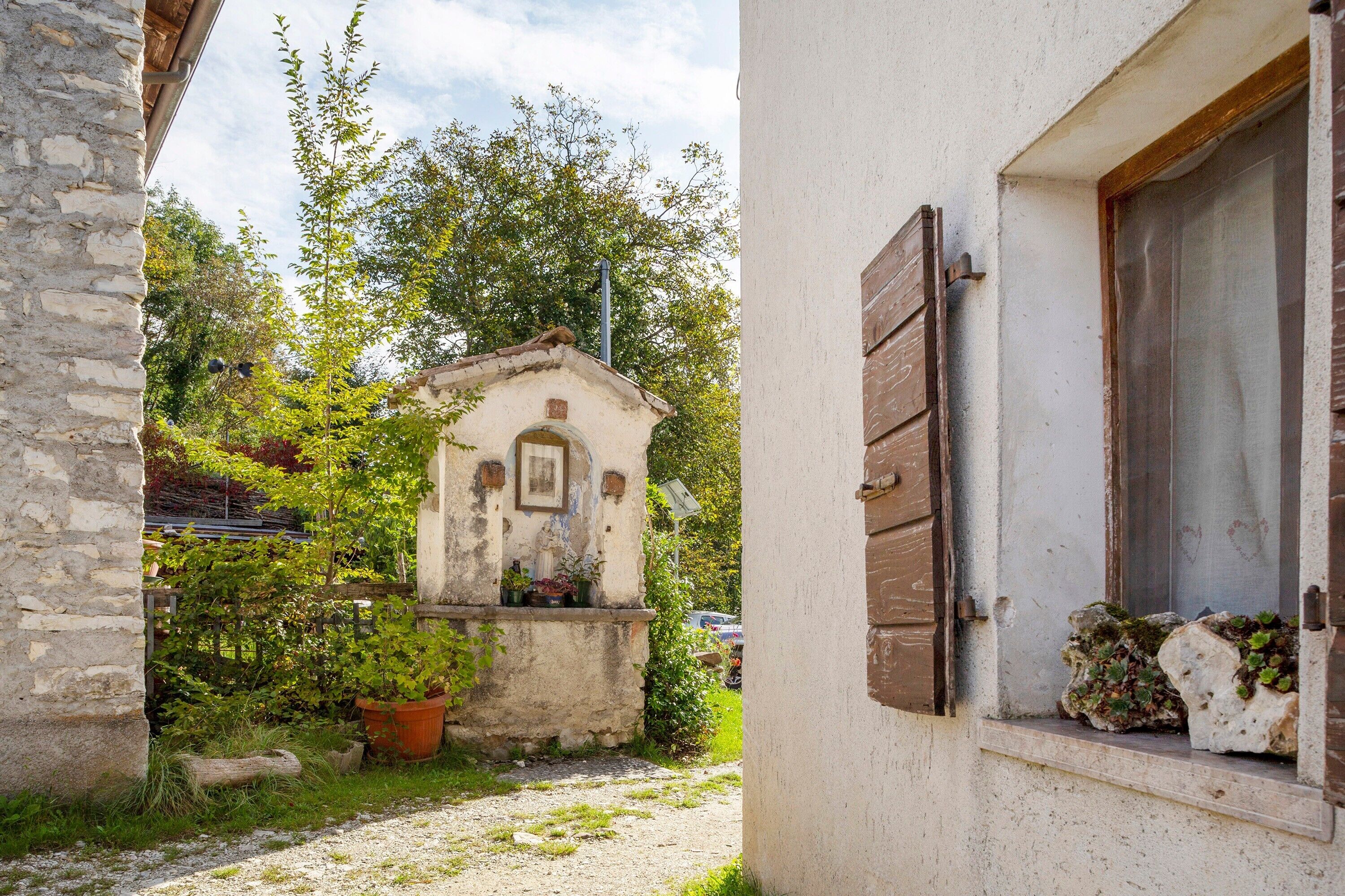 Un callejón estrecho con un edificio rústico, una pequeña construcción con tejado inclinado y una ventana con contraventanas de madera.