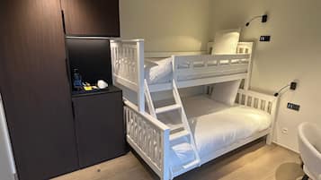 Habitación con literas, un armario oscuro, un estante con objetos y una silla blanca.