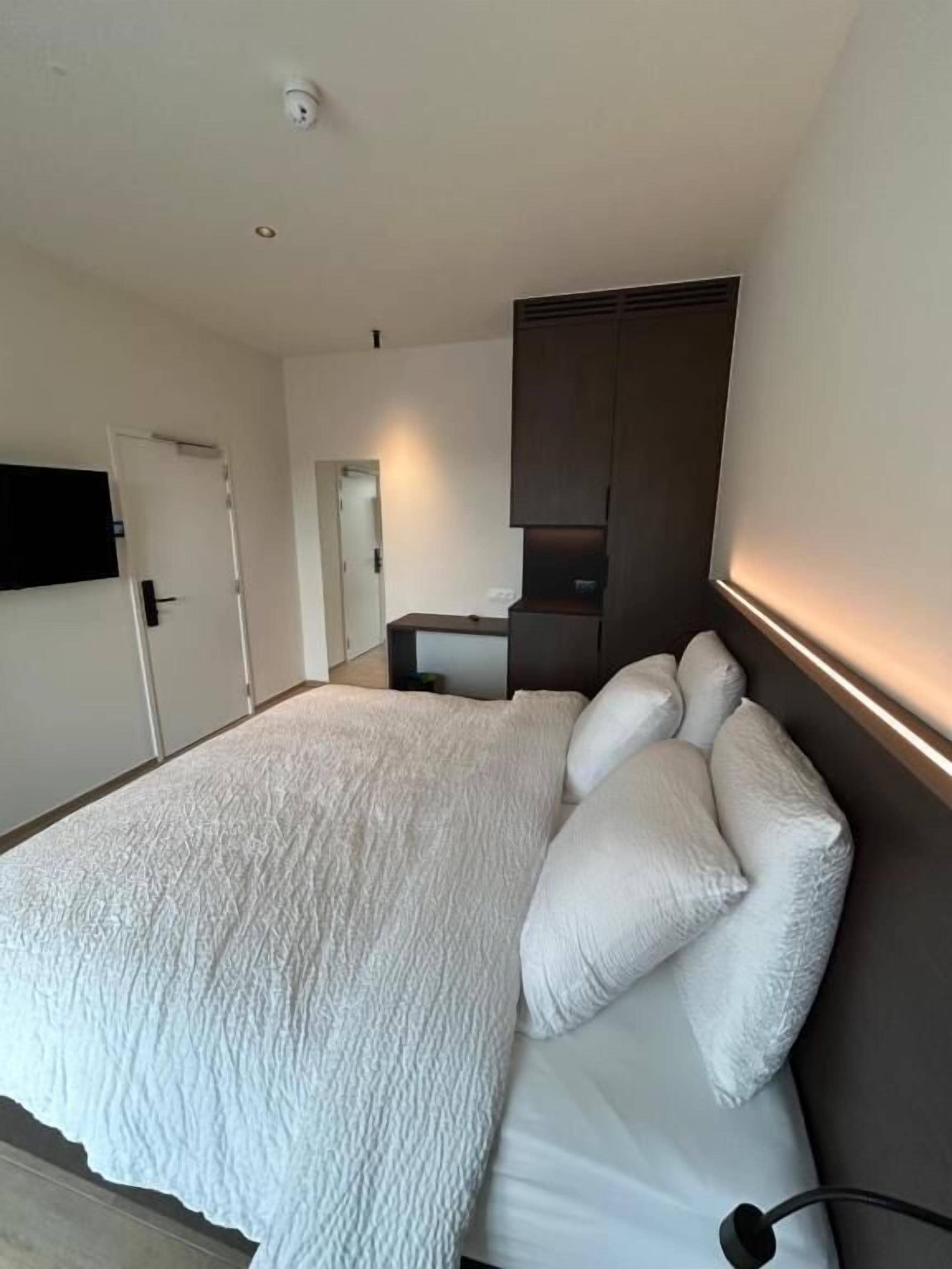 Een moderne slaapkamer met een groot bed, een flatscreen televisie aan de wand en een inbouwkast.