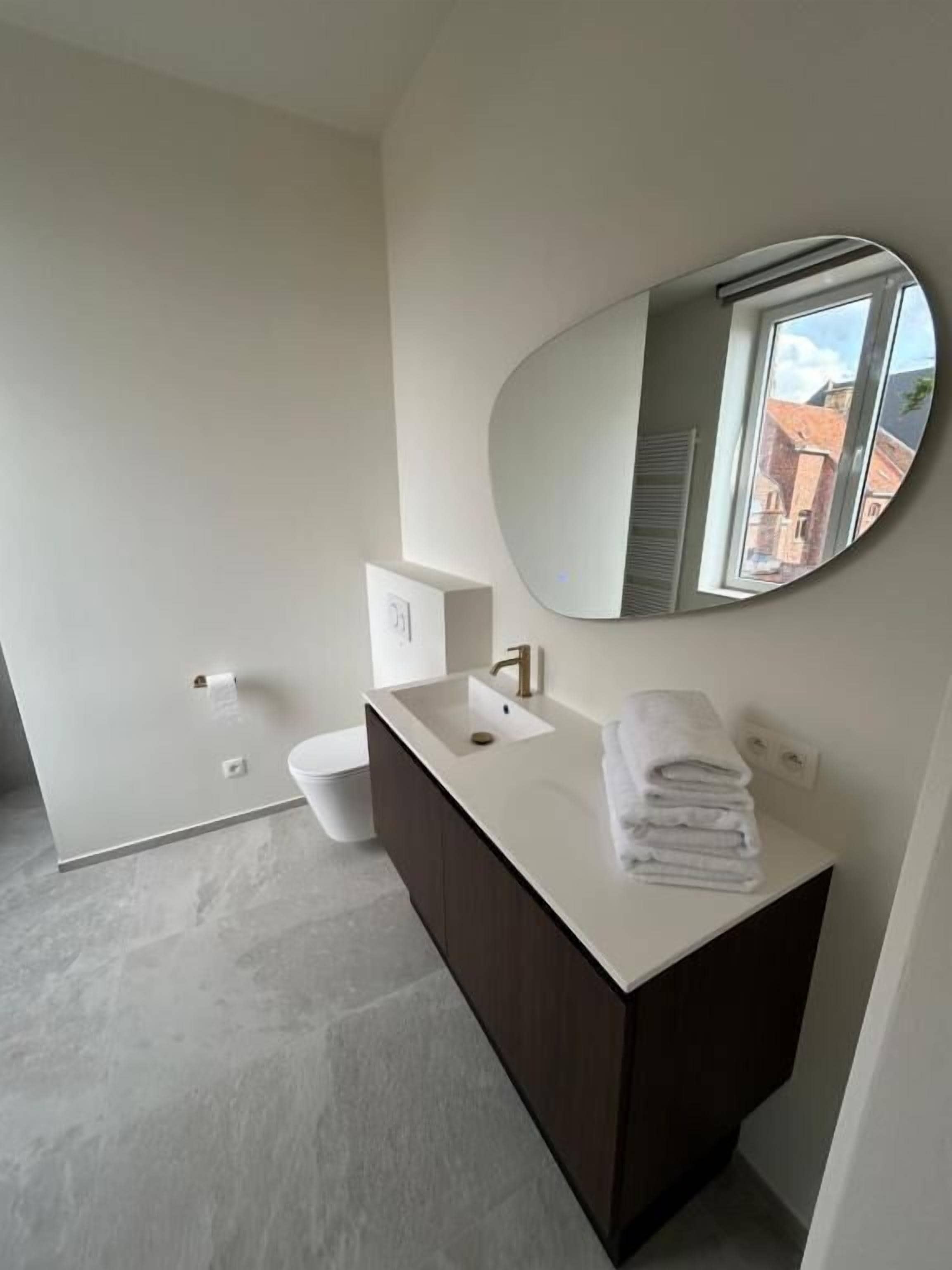 Een moderne badkamer met een wit wastafel, donker kastje en grote spiegel.