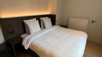 A modern bedroom with a large bed, a bedside table, and a nightstand.