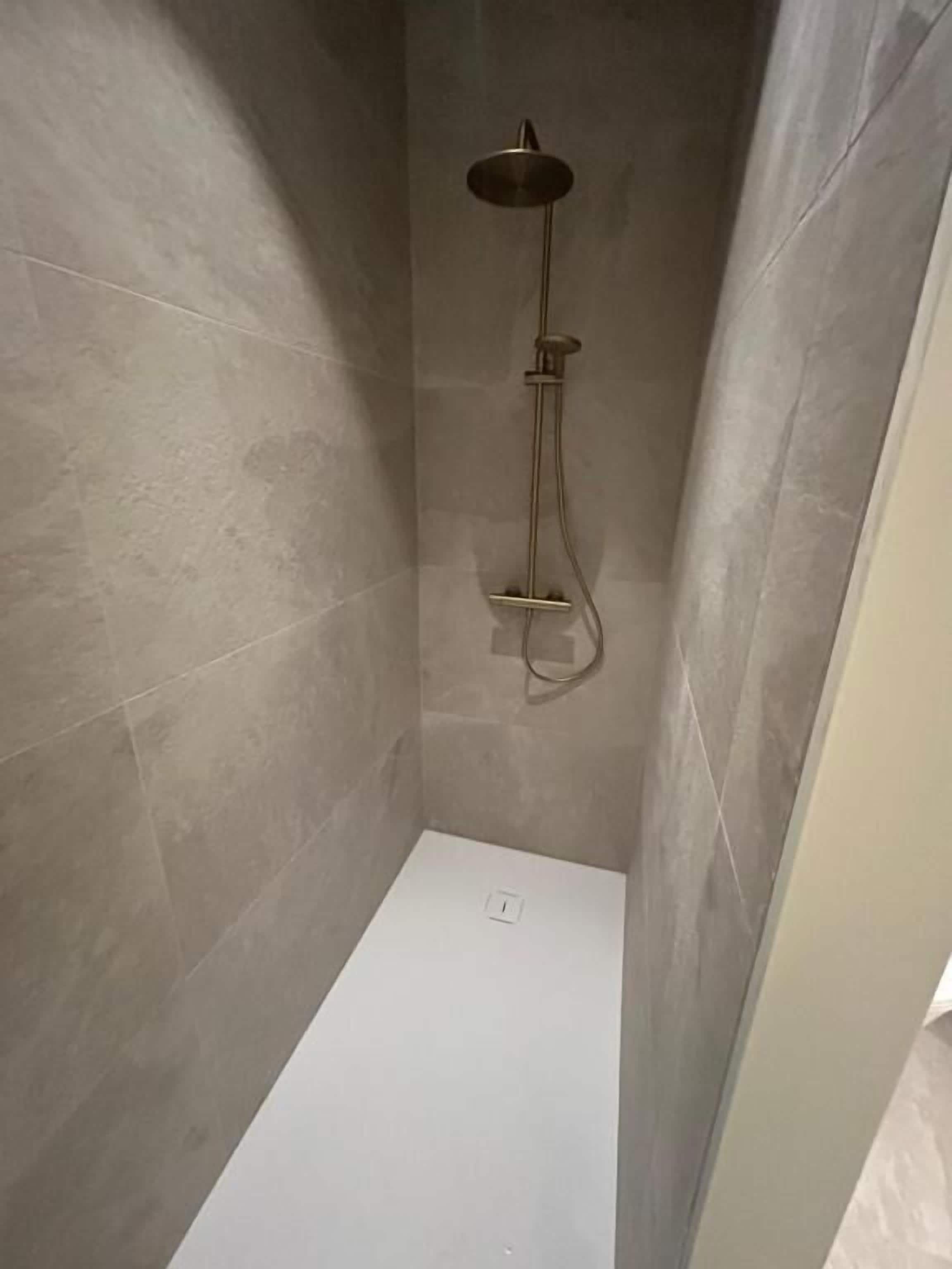 Dutxa amb plat de roba a mà i aixeta fixada a la paret, tot en una habitació amb rajoles.