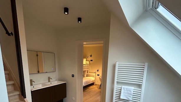 A modern interior with a staircase leading to a bedroom, a bathroom with a large mirror, and a radiator. - Manteka Logies (Ypres)