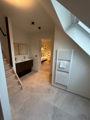 A modern interior with a staircase leading to a bedroom, a bathroom with a large mirror, and a radiator. - Manteka Logies (Ypres)