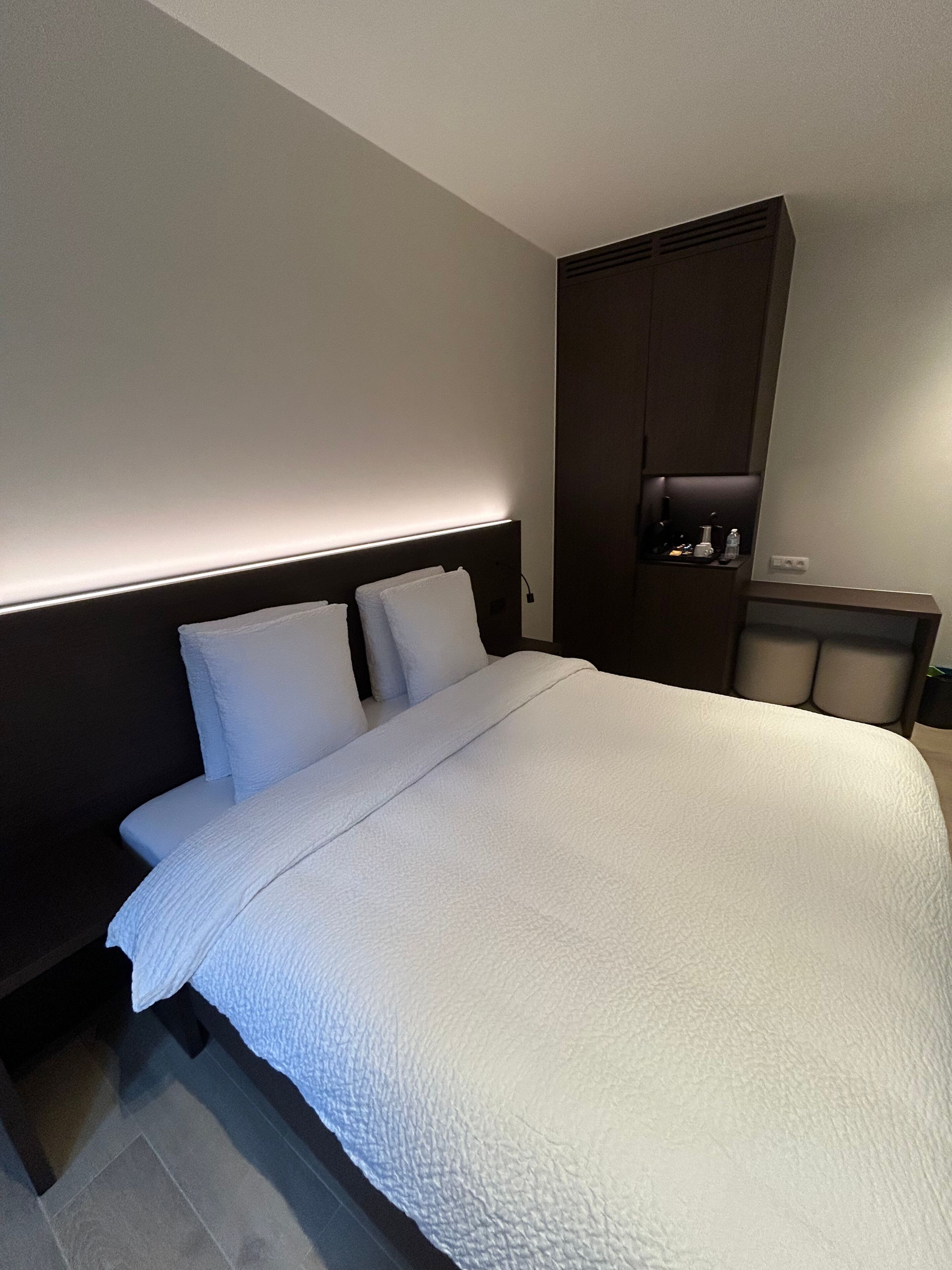 A modern hotel room with a large bed, a dark headboard, and a built-in wardrobe.