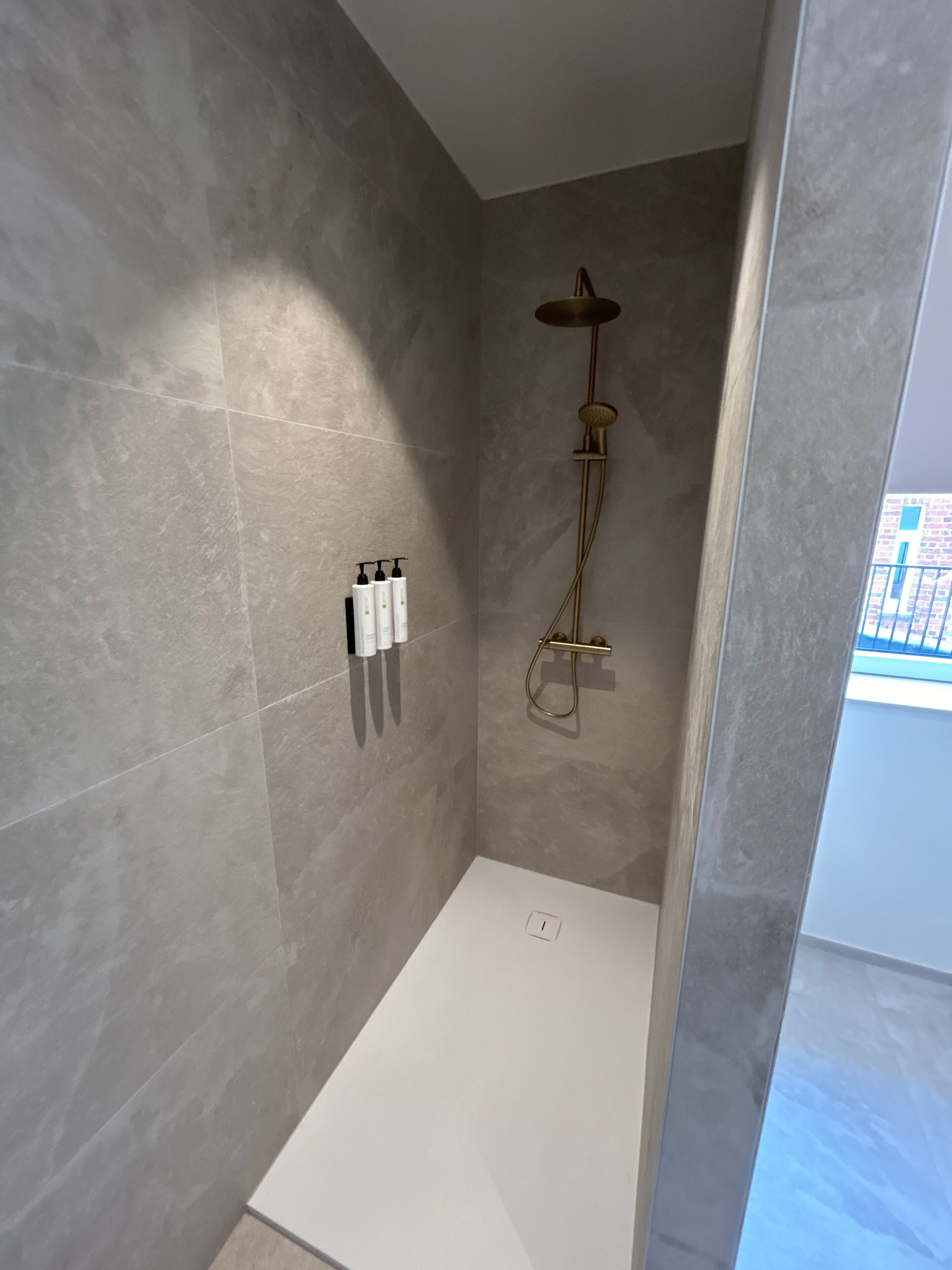 Una ducha moderna con un cabezal de ducha dorado y suelo blanco.