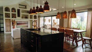 Uma cozinha moderna com ilha central, iluminação pendente e área de jantar com mobiliário de madeira.