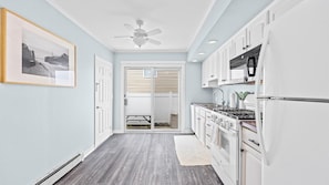 A narrow kitchen with white cabinets, a stove, and a ceiling fan.