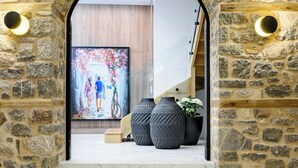 A stone archway leading to a modern interior with a large poster, potted plants, and a staircase.