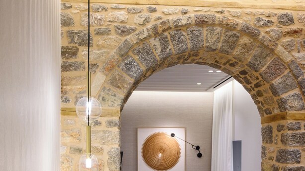 A modern living room with a stone archway, a grey sofa, a coffee table, and a hanging light fixture.