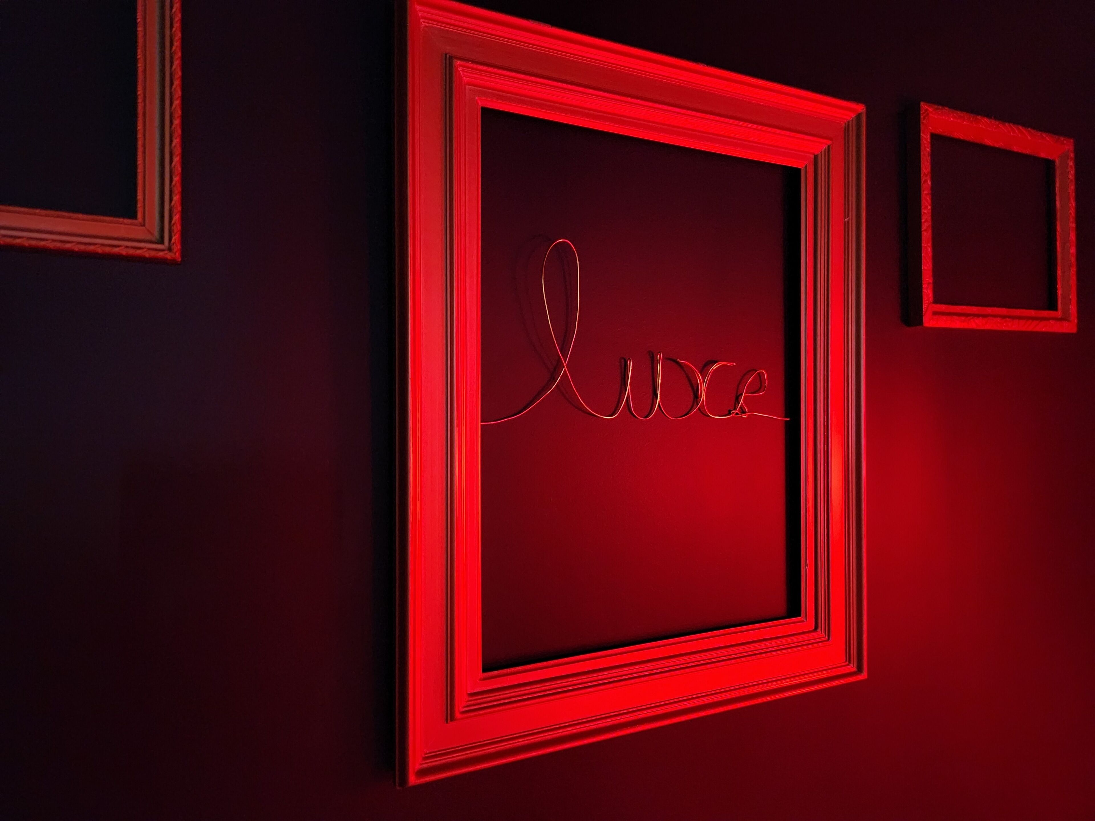Une œuvre d’art encadrée, sur laquelle le mot « LUXE » est écrit en lettres cursives sur un fond sombre.