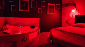 A room with a red-lit jacuzzi, a bed, and framed artwork on the wall. - The Volupté Suite - Luxury, calm and romance with private sauna and Jacuzzi (Doué-en-Anjou)