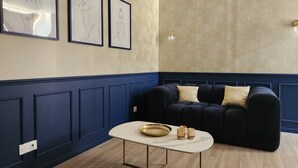 A room with a dark blue upholstered sofa, a white marble coffee table with a gold tray and candle holders, and three framed line drawings on the wall. - The Volupté Suite - Luxury, calm and romance with private sauna and Jacuzzi (Doué-en-Anjou)