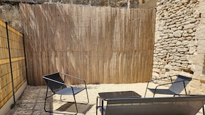 An outdoor seating area with two chairs and a table, a bamboo fence, and a stone wall. - The Volupté Suite - Luxury, calm and romance with private sauna and Jacuzzi (Doué-en-Anjou)