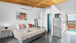 A bedroom with a bed, a nightstand, a wall-mounted air conditioner, a painting, and a view through a window. - Pink Lagoon by Boutique Bonaire Unique Resorts (Kralendijk)