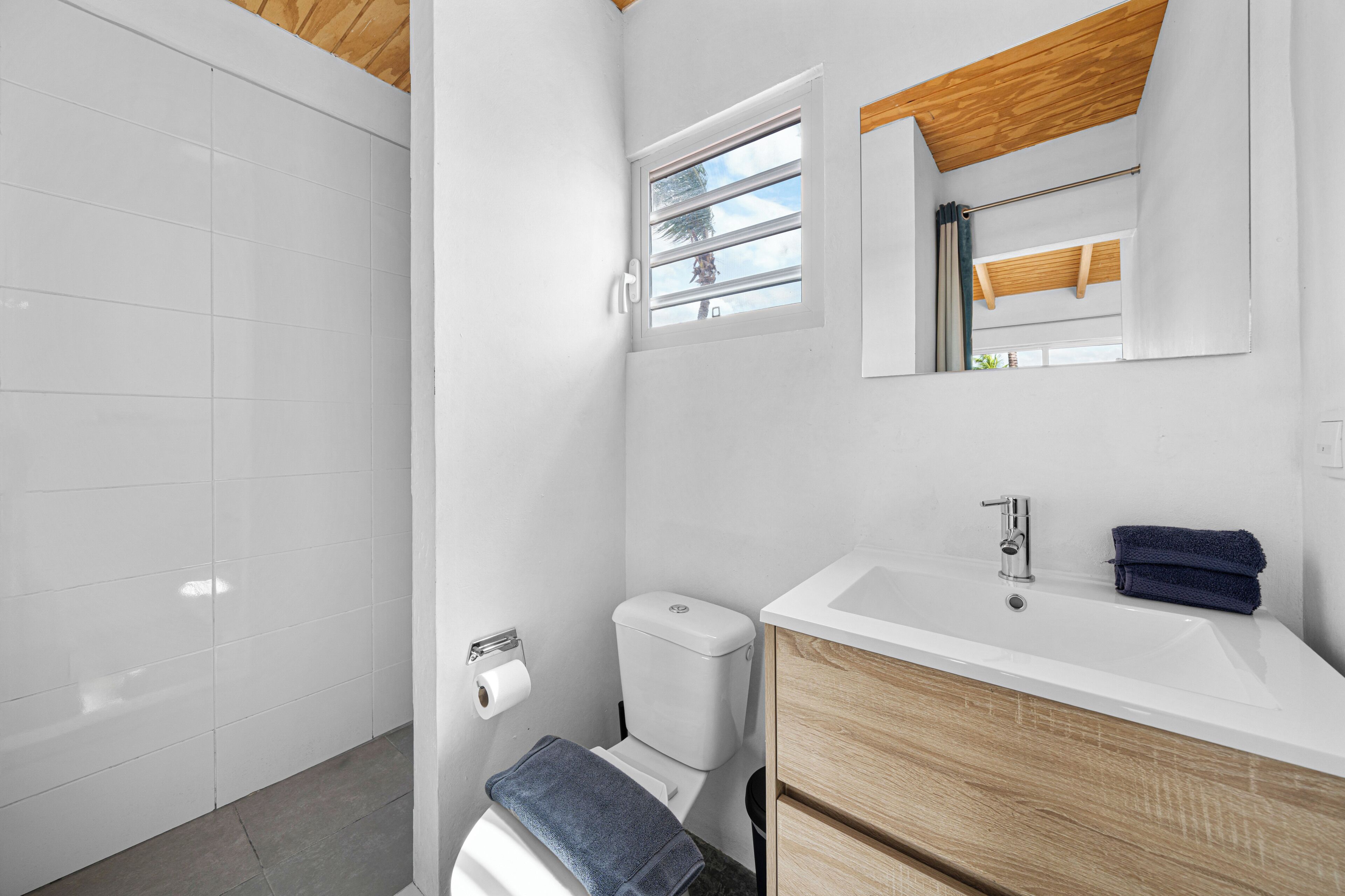 A modern bathroom with a white toilet, a sink with a wooden vanity, a towel, and a window with a view.