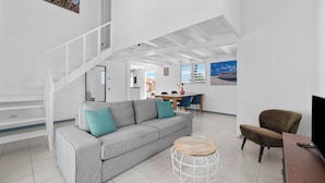 A modern living room with a grey sofa, a round wooden coffee table, a brown armchair, a TV stand, and a staircase leading to another room. - Pink Lagoon by Boutique Bonaire Unique Resorts (Kralendijk)