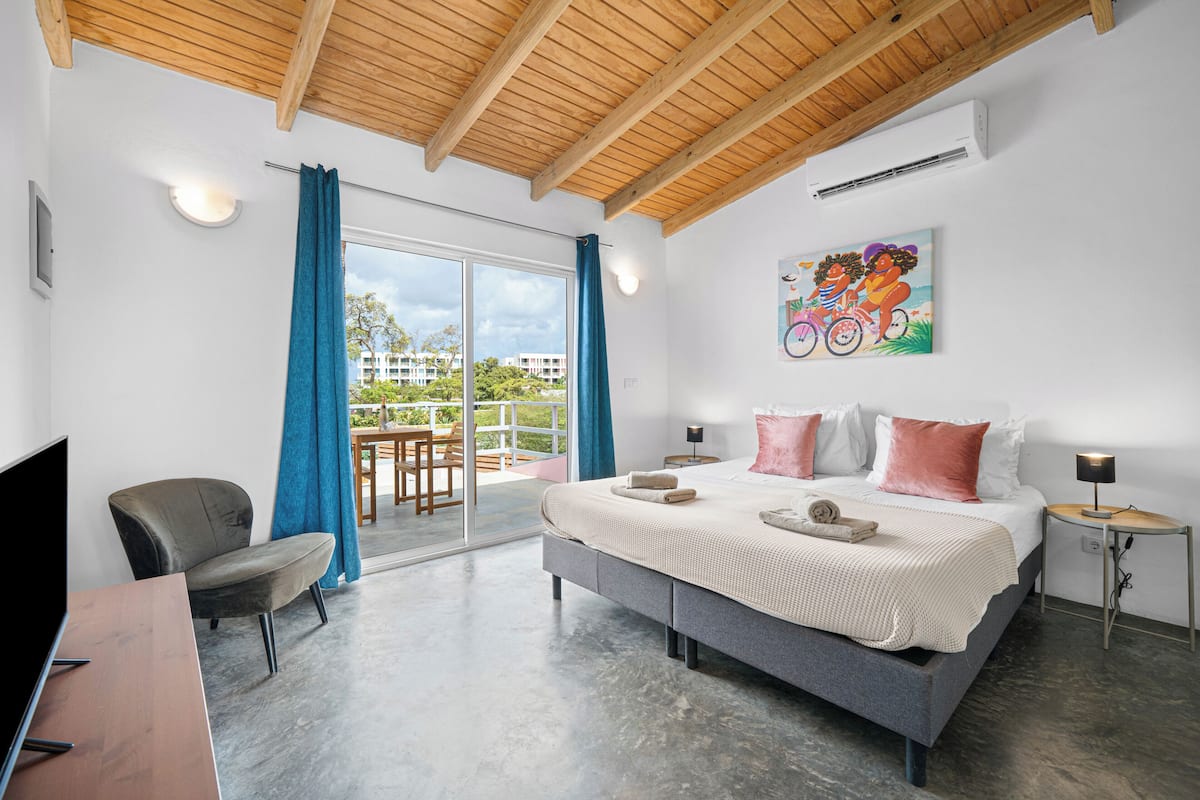 Une chambre d’hôtel moderne avec un grand lit, une télévision, un bureau et un balcon agrémenté de rideaux bleus.