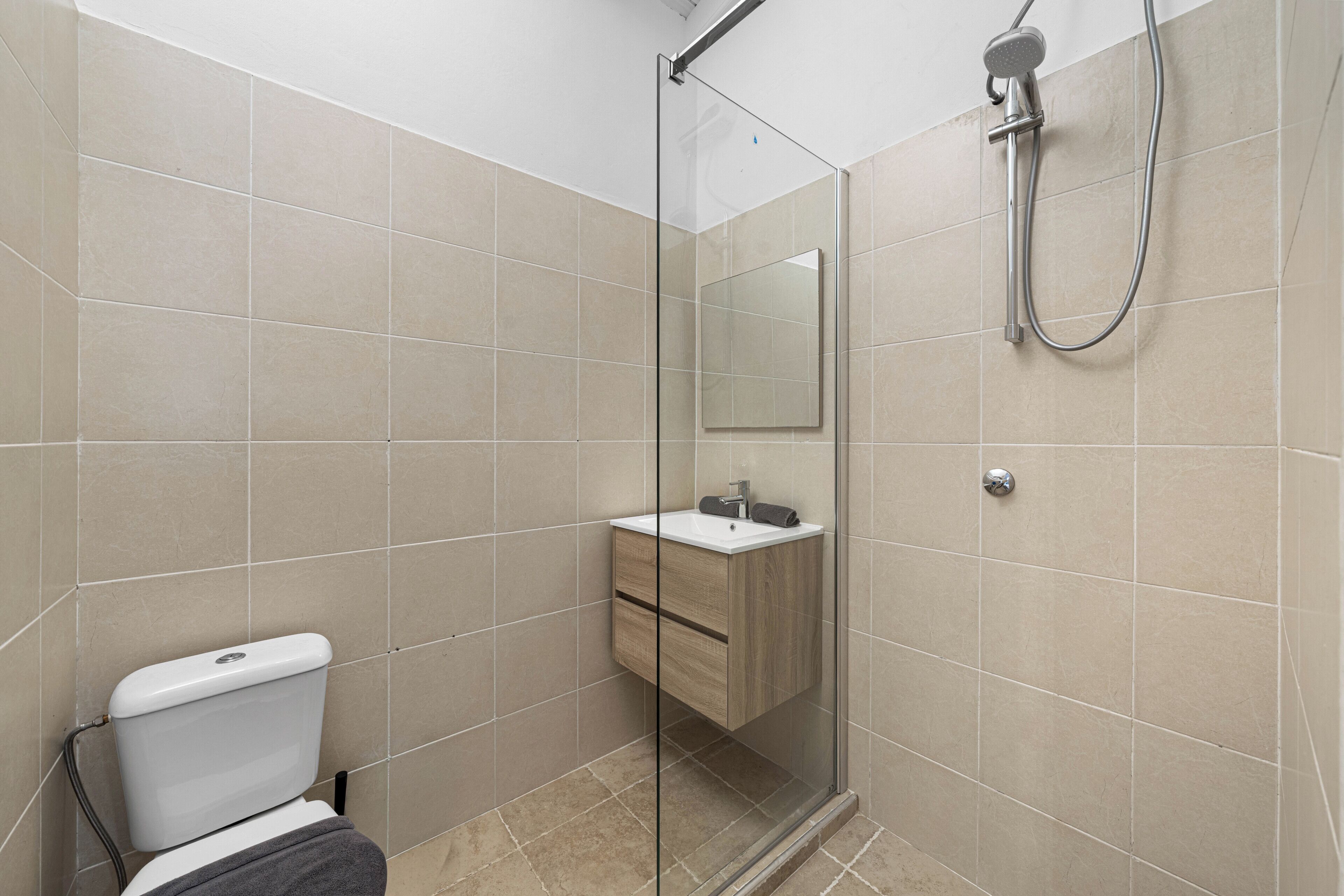 A modern bathroom with a glass shower enclosure, a white toilet, and a wooden vanity with a mirror.