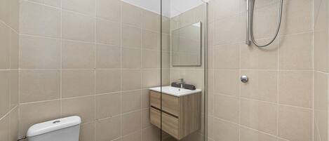 A modern bathroom with a glass shower enclosure, a white toilet, and a wooden vanity with a mirror.