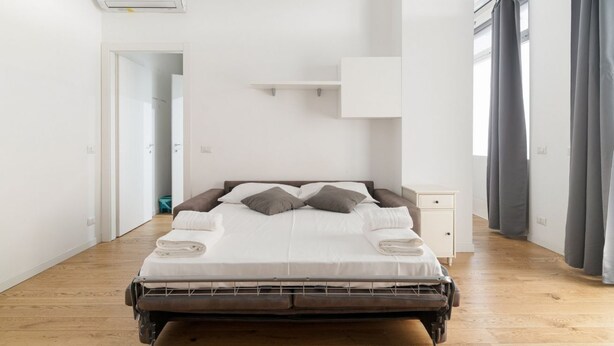 Un dormitorio moderno con cama, una mesita de noche, una estantería en la pared y una ventana con cortinas.