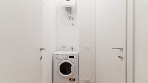 Un lavadero pequeño con lavadora, una lámpara en el techo y una puerta.